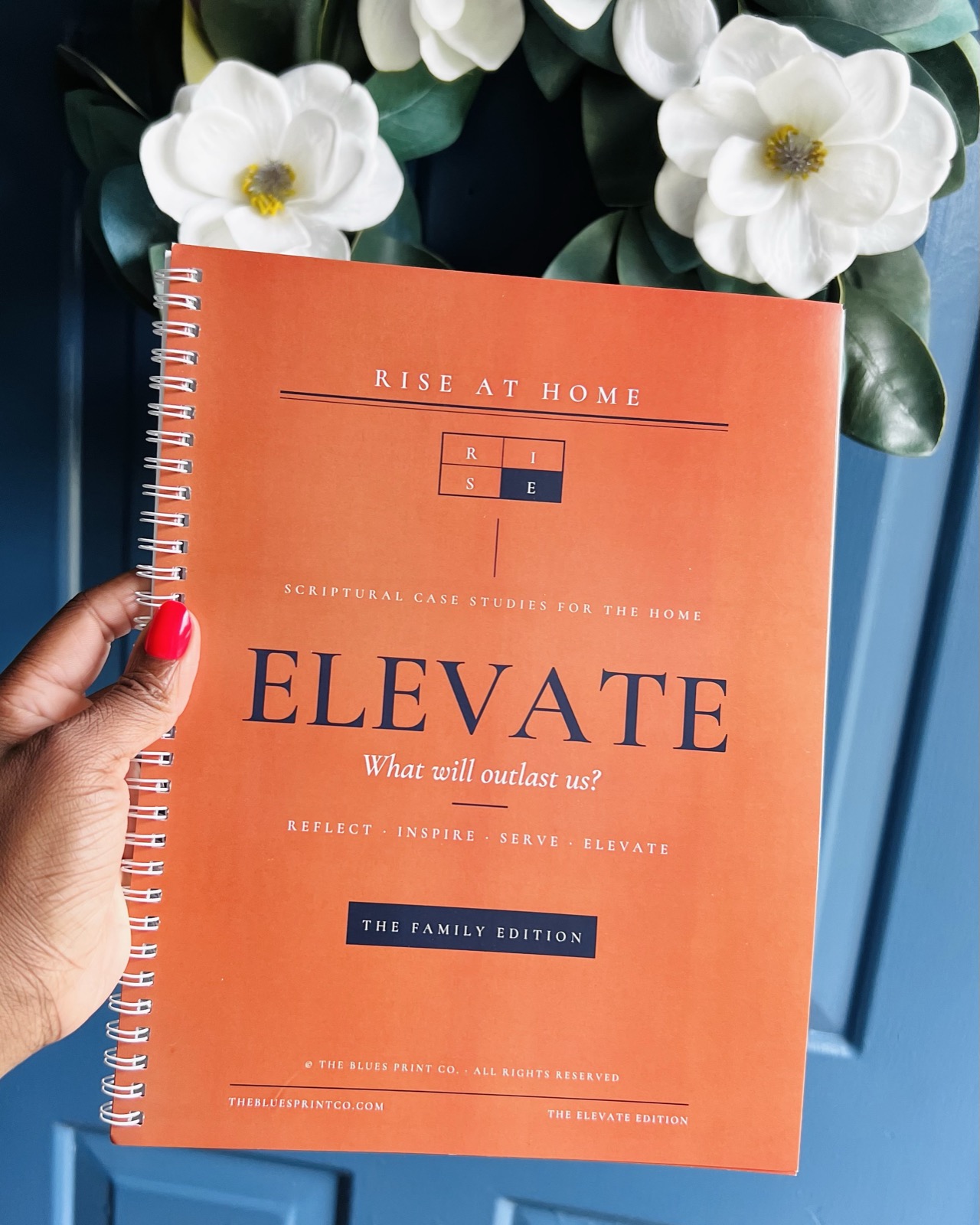 The ELEVATE Family Edition held against a navy door with magnolias
